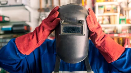 Soudeur portant un masque de protection et des gants de soudure dans un atelier métallurgique, illustrant les opérations de maintien et d'assemblage de pièces avant soudage.