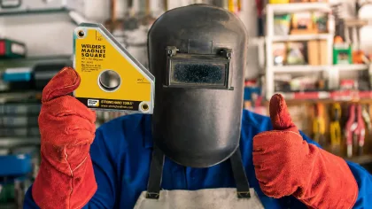 Soudeur équipé d'un masque de protection tenant une équerre magnétique de soudure dans un atelier de fabrication métallique.